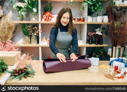 Female seller wraps carton gift box in festive paper. Present wrapping on the table, decoration procedure. Female seller wraps gift box in festive paper