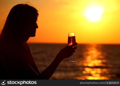 Female silhouette on sea sunset with glass in hand