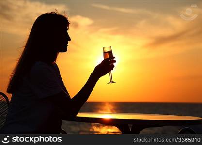 Female silhouette on sunset at table with glass in hand