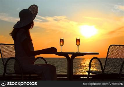 Female silhouette on sunset behind table with two glasses