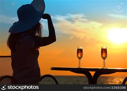 Female silhouette on sunset behind table with two glasses