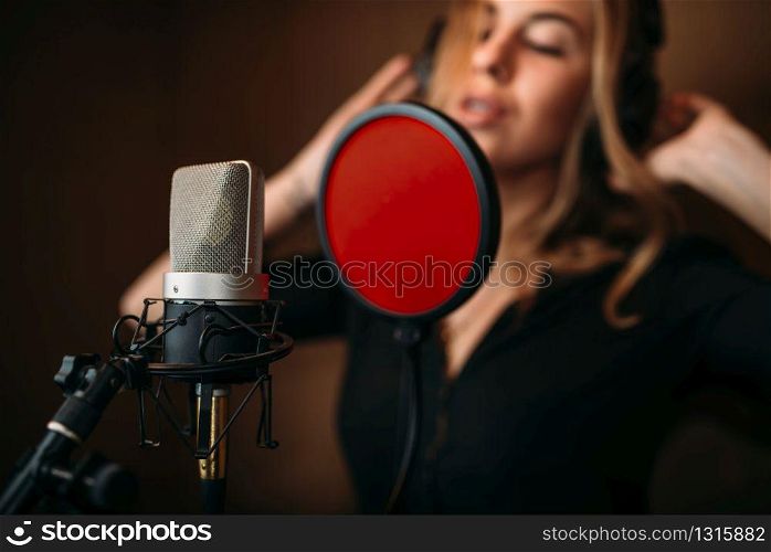 Female singer in headphones against microphone, song record in music studio. Woman vocalist . Audio recording. Professional digital sound technologies