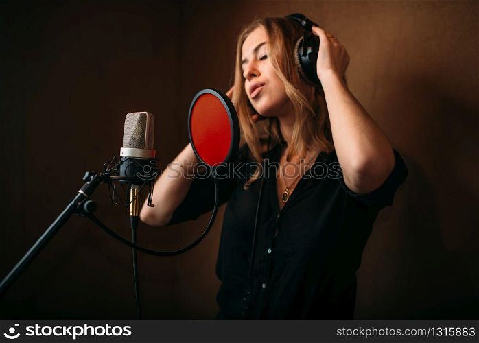 Female singer in headphones against microphone, song record in music studio. Woman vocalist . Audio recording. Professional digital sound technologies. Female singer in headphones against microphone
