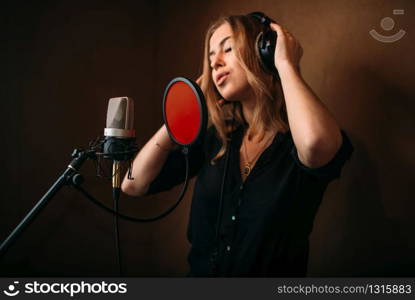 Female singer in headphones against microphone, song record in music studio. Woman vocalist . Audio recording. Professional digital sound technologies. Female singer in headphones against microphone