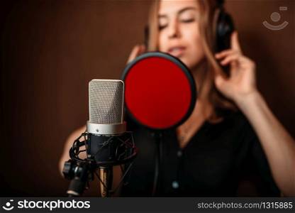 Female singer in headphones against microphone, song record in music studio. Woman vocalist . Audio recording. Professional digital sound technologies. Female singer in headphones against microphone