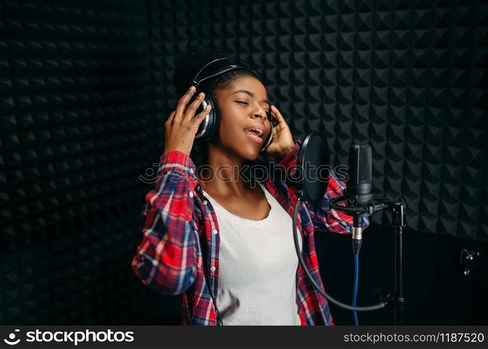 Female singer in headphones songs in audio recording studio. Musician listens composition, professional music. Female singer songs in audio recording studio