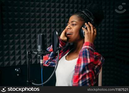 Female singer in headphones songs in audio recording studio. Musician listens composition, professional music mixing