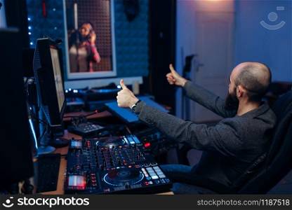 Female singer in recording room and sound engineer and at remote control panel in studio. Musician in headphones listens composition, professional music mixing. Female singer in recording room and sound engineer