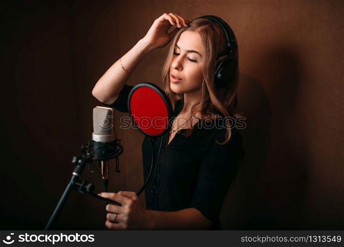 Female singer recording a song in music studio. Woman vocalist in headphones against microphone. Audio recording. Professional digital sound technologies