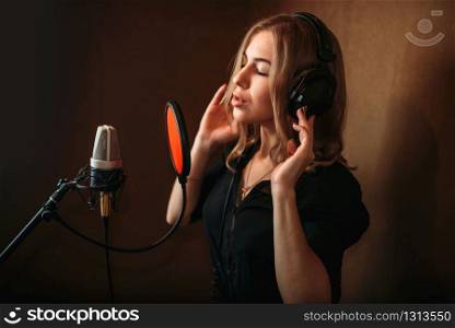 Female singer recording a song in music studio. Woman vocalist in headphones against microphone. Audio recording. Professional digital sound technologies. Female singer recording a song in music studio