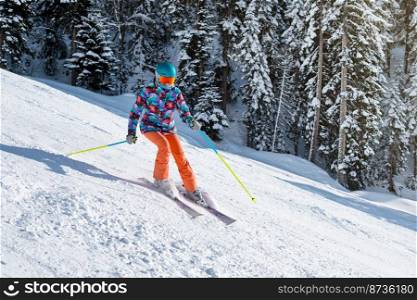 Female skier in bright clothes sliding down the slope on a sunny day at a mountain resort.