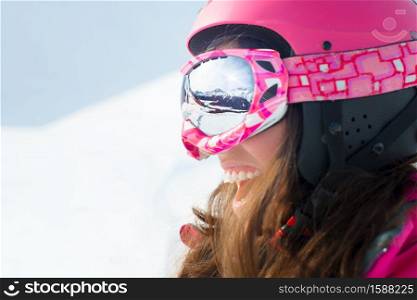 Female skier with skis smiling and wearing ski glasses. With reflection panorama of mountains