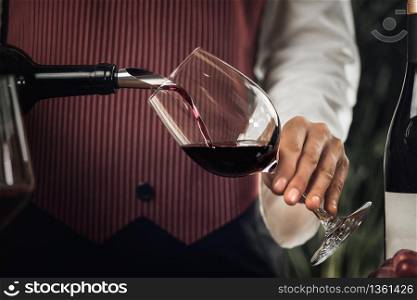 Female sommelier pouring red wine into wine glass.