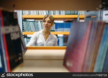 Female student choosing book at the bookshelf in university library. Young woman in reading room, knowledge depository