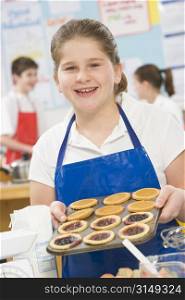 Female student holding a tray of tarts in cooking class