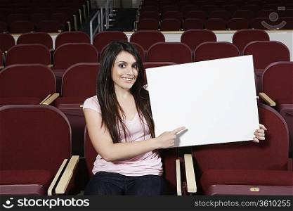 Female student holding blank board in lecture theatre, portrait