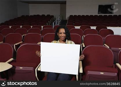 Female student holding blank board in lecture theatre, portrait