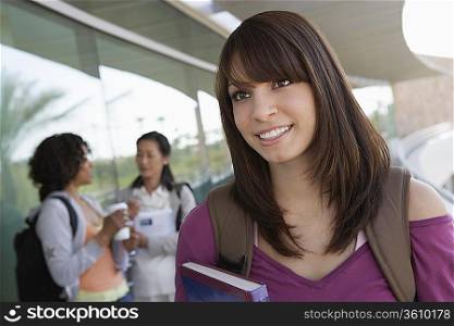 Female student holding book at school, smiling