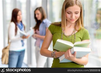 Female student reading book at high school library glass hall