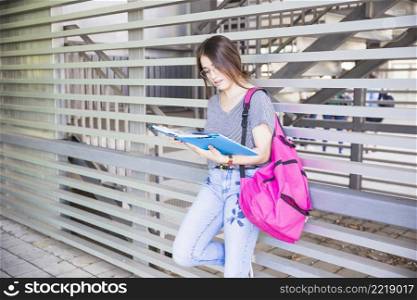 female student reading textbook near wall