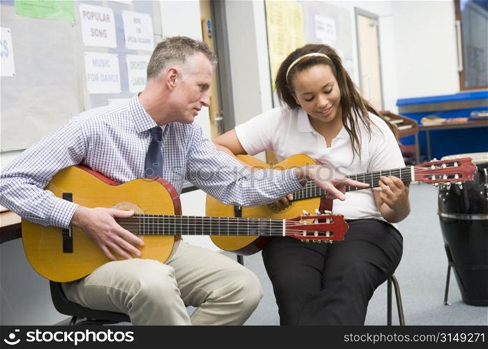 Female student receiving guitar lesson from teacher in classroom