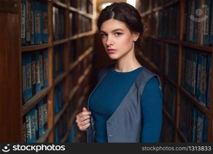 Female student standing between bookshelves in library.