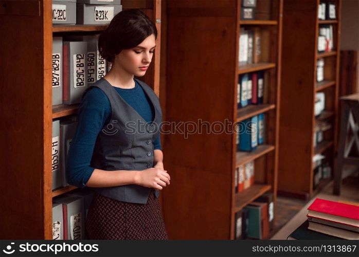 Female student standing with eyes closed in college library. Bookshelf with books and textbooks on the background.. Student standing with eyes closed in library.