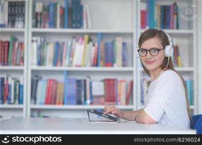 female student study in library using tablet and searching internet while Listening music and lessons on white headphones