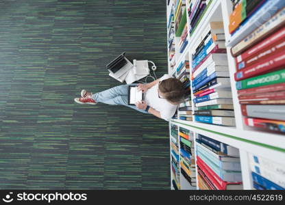 female student study in school library, using tablet and searching for information?s on internet. Listening music and lessons on white headphones