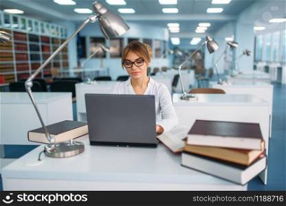 Female student studying at the laptop in library. Young woman in reading room, knowledge depository