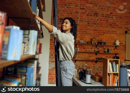 Female student takes book from shelf in university library. Woman at bookshelf, education and knowledge. Girl studying in campus. Female student takes book from shelf in library