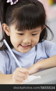 Female Student Working At Desk In Chinese School Classroom