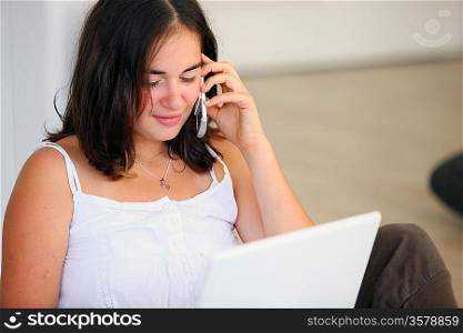 female student working on laptop using cell phone