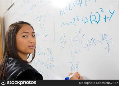 Female student writing maths equations on whiteboard