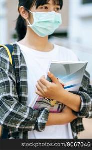 Female students wear masks, stand on stairs and hold books.