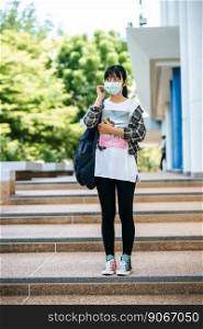 Female students wear masks, stand on stairs and hold books.