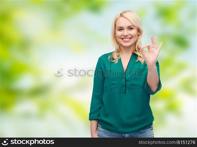 female, summer, gesture, plus size and people concept - smiling young woman in shirt and jeans showing ok hand sign over green natural background