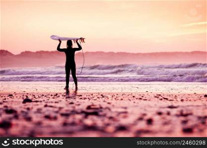 Female surfer on the beach at the sunset