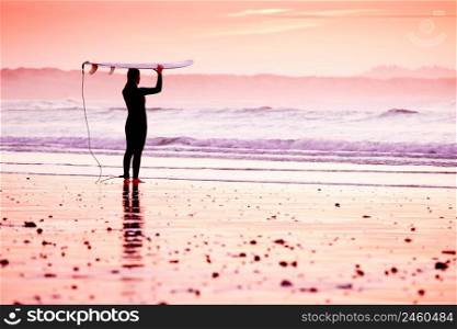 Female surfer on the beach at the sunset