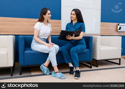 Female surgeon and patient sitting on sofa in clinic hall, surgery. Doctor in uniform, medical worker, medicine and health, professional healthcare in hospital. Surgeon and patient are sitting on sofa in clinic