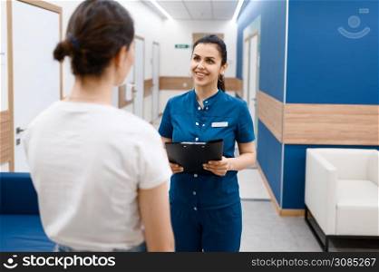 Female surgeon talks with patient in clinic hall, surgery. Doctor in uniform, medical worker, medicine and health, professional healthcare in hospital. Female surgeon talks with patient in clinic hall