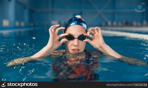 Female swimmer in swimsuit, swimming cap and glasses poses in pool. The woman at the poolside, aqua aerobics training, healthy lifestyle. Female swimmer in pool, woman at the poolside