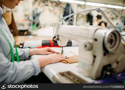 Female tailor hands sews fabrics on a sewing machine. Tailoring or dressmaking on clothing factory, needlework, seamstress in workshop. Tailor hands sews fabrics on a sewing machine