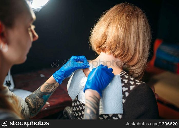 Female tattoo artist in blue sterile gloves prepares client skin for tattooing. Tattoo salon. Tattoo artist prepares client skin for tattooing