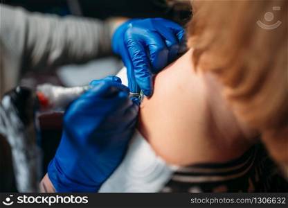 Female tattooer in blue sterile gloves makes tattoo by machine, master in salon. Professional tattooing process in studio. Female tattooer makes tattoo by machine