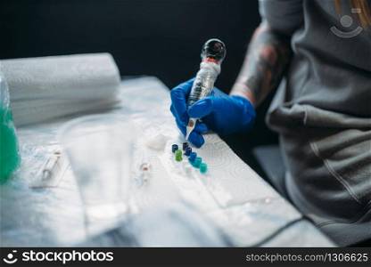 Female tattooist hands in blue sterile gloves holds tattoo machine, professional work tools on background. Tattooing in salon. Female tattooist hands holds tattoo machine