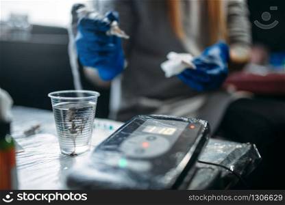 Female tattooist hands in blue sterile gloves holds tattoo machine, professional work tools on background. Tattooing in salon. Female tattooist hands holds tattoo machine