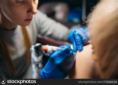 Female tattooist in blue sterile gloves makes tattoo by machine, master in salon. Professional tattooing process in studio