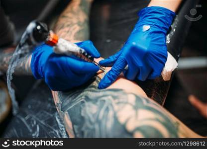 Female tattooist makes tattoo by machine on male shoulder. Professional tattooing in salon. Tattooist makes tattoo by machine on male shoulder