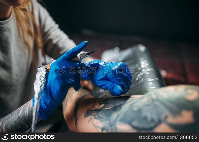 Female tattooist makes tattoo by machine on the shoulder. Professional tattooing in salon. Tattooist makes tattoo by machine on male shoulder